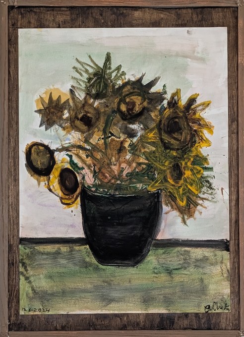 Drooping yellow sunflowers and green leaves in a black vase on a green tabletop.