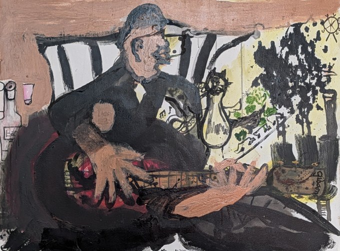 Seated musician holding a guitar across the lap in an interior with black and white stripes.